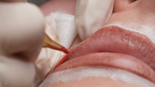 Microblading lip tattoo with a special coloring red pigment that corrects lip color in a cosmetology clinic. Permanent makeup lips procedure applying pigment makeup on lips with a tattoo machine close - Footage, Video