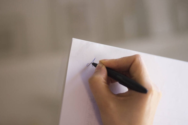 Mladá dáma píše na papír s tužkou v ruce na stůl. - Fotografie, Obrázek