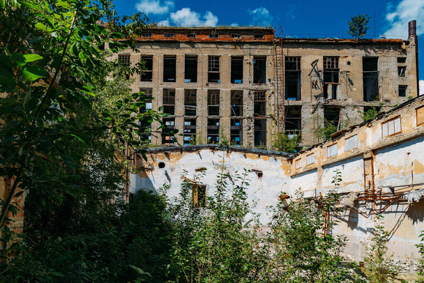 Old abandoned ruined industrial building overgrown by plants and trees. - Fotografie, Obrázek