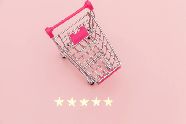 Pequeño supermercado carrito de compras empuje para juguete de compras con ruedas y clasificación de 5 estrellas aislado sobre fondo rosa pastel. Compras al por menor concepto de evaluación y revisión en línea
 - Foto, Imagen