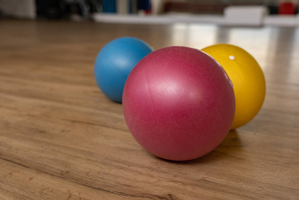 Tres pequeñas y coloridas bolas de gimnasia en el suelo de madera de una sala de gimnasia de un gimnasio de grupo. Reflejos de espejo en el fondo. Vista de ángulo bajo
. - Foto, Imagen