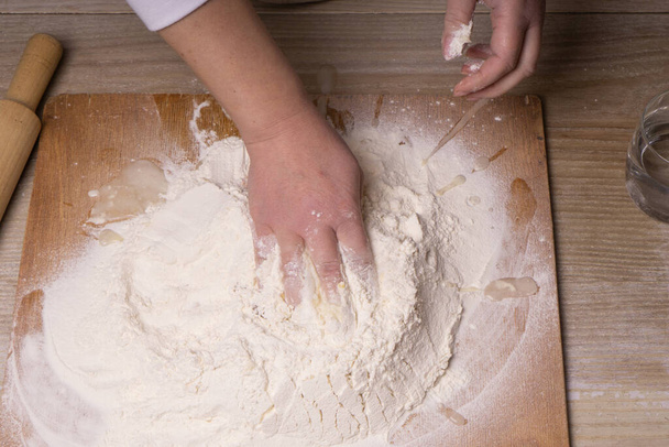 Une femme pétrit la pâte. Panneau à découper en contreplaqué, tamis à farine en bois et rouleau à pâtisserie en bois - outils pour fabriquer la pâte
 - Photo, image