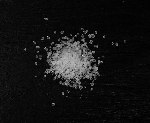 Velké krystaly cukru na černém pozadí zblízka. Makro snímek krystalů sacharózy, mořské soli horniny nebo granulované sodné soli textury na potravinové břidlice horní pohled - Fotografie, Obrázek
