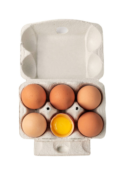 Offene Schachtel mit sechs ganzen braunen Eiern und einem gebrochenen Ei isoliert auf weißem Hintergrund mit Clip-Pfad. Frische Bio-Hühnereier im Karton oder Eierbehälter von oben - Foto, Bild