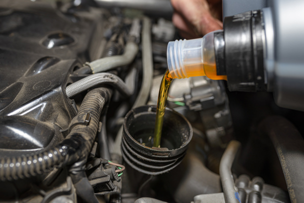 Mécanicien automobile verse de l'huile de voiture neuve dans le moteur à partir d'un réservoir en plastique dans un atelier de voiture. - Photo, image