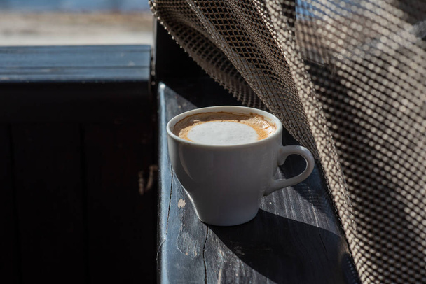 Koffie selectieve focus. Witte beker met cappuccino op de natuur. Witte beker met cappuccino, koffie, 's morgens, vrolijkheid. - Foto, afbeelding
