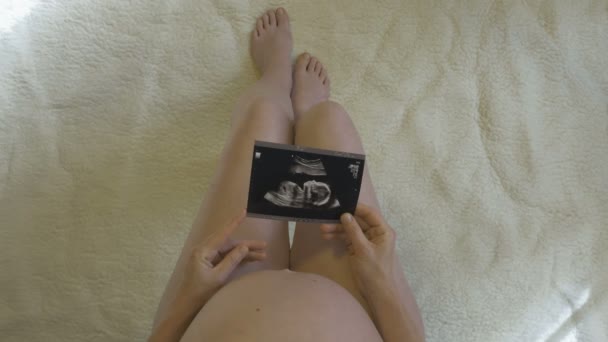 Raskaana oleva nainen katsoo valokuvaa syntymättömästä lapsestaan - Materiaali, video