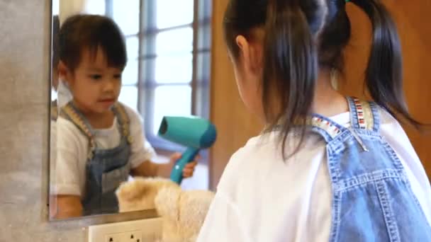 Cute uśmiechnięta dziewczynka gra suszarkę do włosów z pluszową lalką w lustrze w pokoju. - Materiał filmowy, wideo