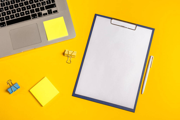 Flat lay out. Computer on yellow background with paper clips, folio, pen and sticky notes. Business concept idea. Copy space. - 写真・画像