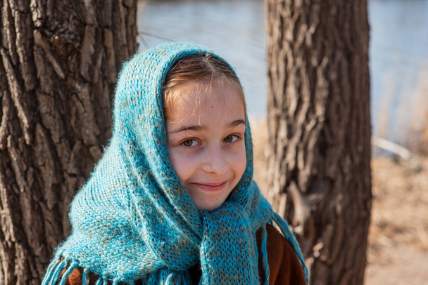 Ένα κορίτσι με ανοιχτόχρωμο παλτό στέκεται στην όχθη του ποταμού μια ηλιόλουστη μέρα. Ένα κορίτσι 9 ετών με ένα παλτό από δέρμα προβάτου δίπλα στο ποτάμι. Κορίτσι 9 ετών ή 10 ετών. Φύση, παιδί, μαθητριούλα. Έφηβος. - Φωτογραφία, εικόνα
