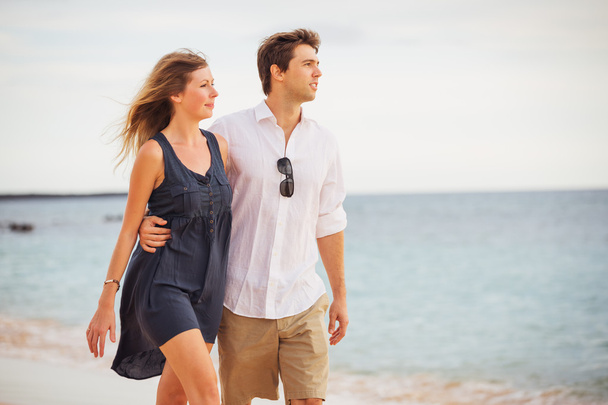 Romantic happy couple walking on beach at sunset. Smiling holdin - 写真・画像
