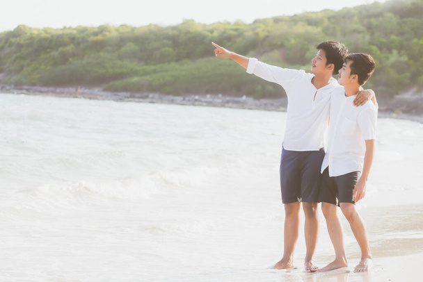 Homosexual retrato joven asiático pareja de pie apuntando algo juntos en la playa en verano, asia gay ir mar para el ocio con romántico y feliz en vacaciones en el mar, LGBT con concepto legal
. - Foto, imagen