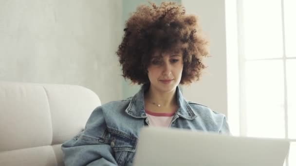 Woman with curly hair writing message in social media on laptop sitting on sofa. - Metraje, vídeo