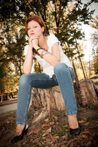 krásná rusovláska dívka v bílé tričko a džíny sedí na pařezu - Fotografie, Obrázek
