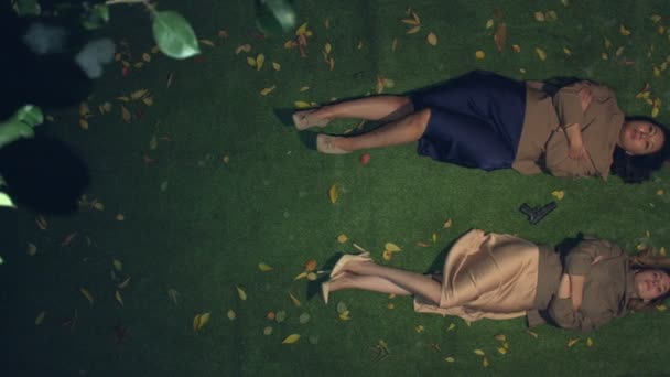 Two women on the grass. Slow motion 2.4x. Top view.Asian and caucasian women lie on the grass among yellow leaves. Between them is a gun. Evening.The camera moves from left to right. - Materiaali, video