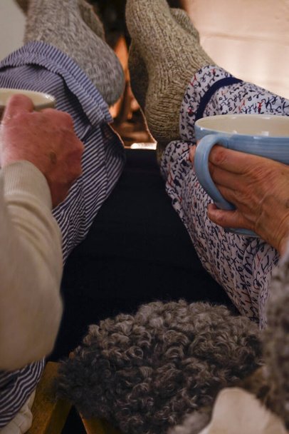 Estocolmo, Suecia Una pareja se sienta a tomar té con calcetines de lana frente a la chimenea
. - Foto, Imagen