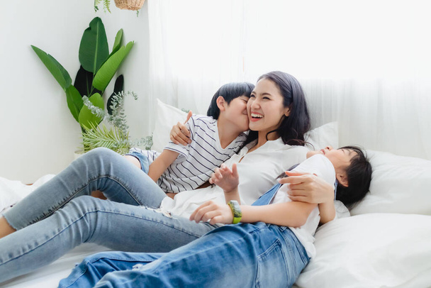 Heerlijk gelukkig Aziatisch gezin in gezellig huis. Zoon en dochter kussen moeder met genieten, ontspannen en speels samen in de slaapkamer. Geluksrelatie en hechting van liefde tussen ouders en kinderen - Foto, afbeelding
