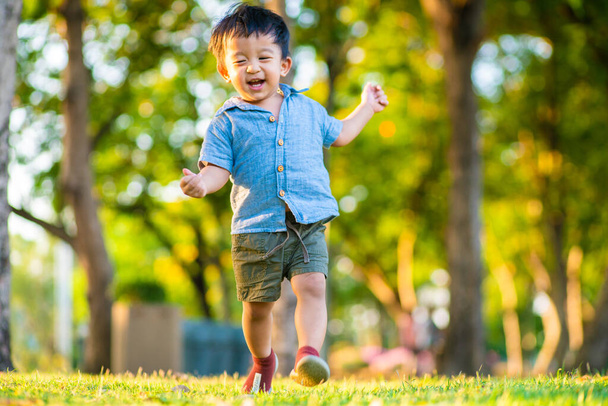 Happy toddler little boy first running on green grass field sunset light in city park outdoor - Фото, изображение