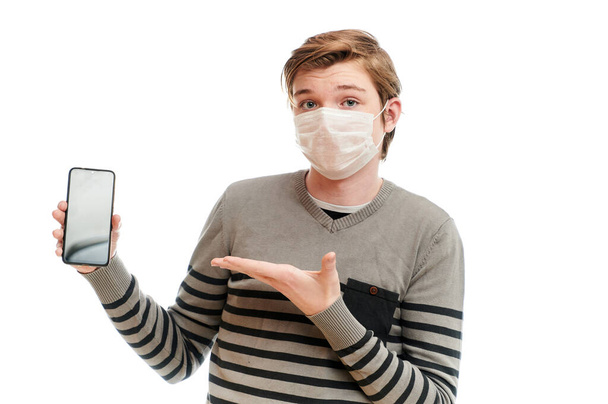 Photo isolate Caucasian guy in a medical mask with a smartphone in his hands - Foto, Bild