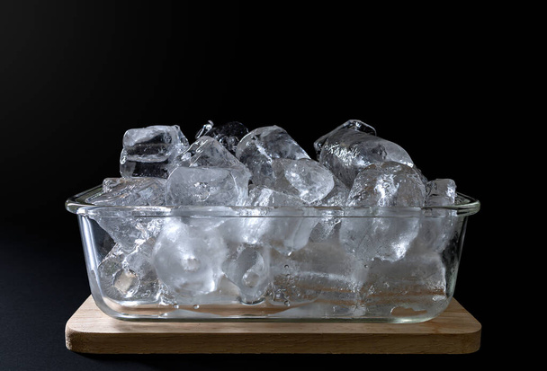Eis in einer Glasschale auf einem hölzernen Tablett auf schwarzem Hintergrund. - Foto, Bild