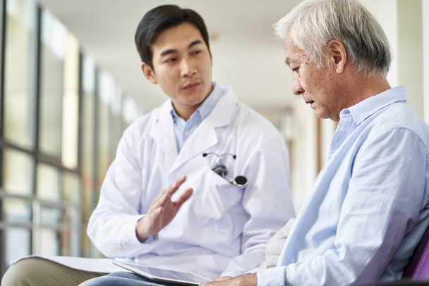 joven asiático médico hablando y explicando prueba resultado y diagnóstico a desmoralizado anciano paciente en hospital pasillo
 - Foto, Imagen
