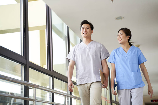 gelukkig jong aziatisch fysiotherapeuten lopen praten in hal van verpleeghuis - Foto, afbeelding