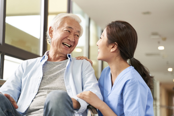 fiatal barátságos ázsiai női gondozó beszélget boldog idősebb férfi folyosón idősek otthon - Fotó, kép