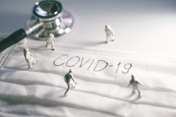 Personas en miniatura médicos con traje protector de prevención de pandemia Covid-19 y Coronavirus, máscara quirúrgica con texto Covid-19 escrito en él con estetoscopio, dramático tonificado
 - Foto, imagen