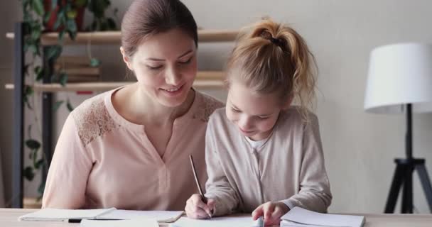 Happy young mum helping cute school child daughter doing homework - Filmagem, Vídeo