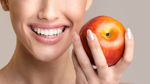 Unrecognizable Girl With Perfect Teeth Holding Apple Smiling, Beige Background - Fotó, kép