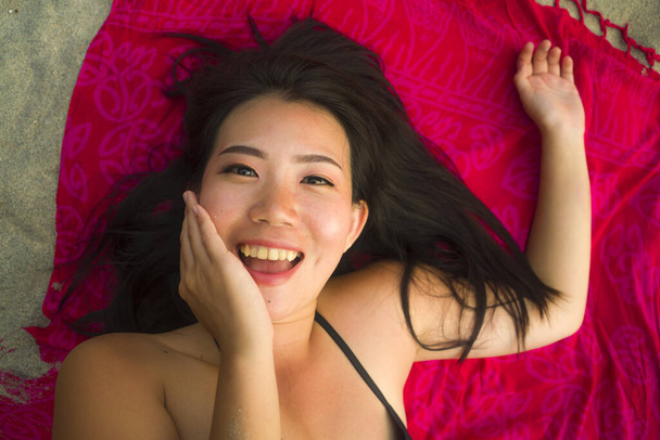 outdoors fresh and natural portrait of young beautiful and happy Asian Cchinese woman in bikini lying flat on sarong on beach sand smiling cheerful and relaxed in beauty and fashion concept - Photo, Image