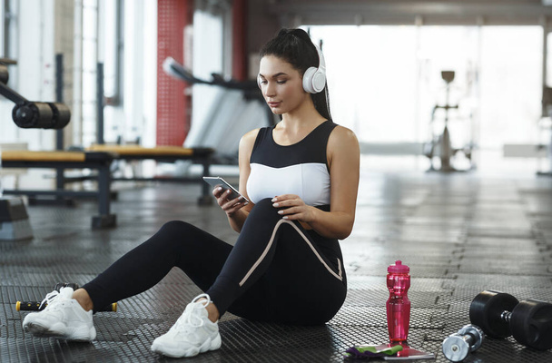 Chica joven con auriculares escuchando música desde el teléfono inteligente en el gimnasio
 - Foto, imagen