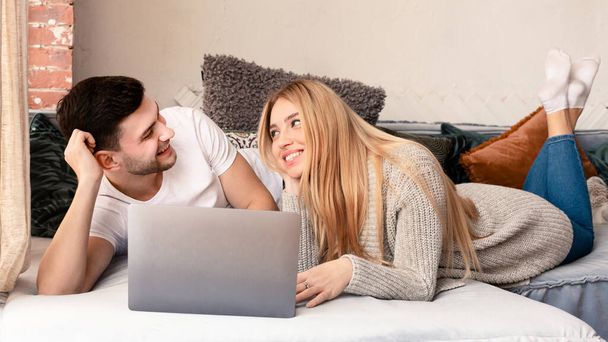 Movie time. Young spouses with laptop resting on sofa at home - 写真・画像