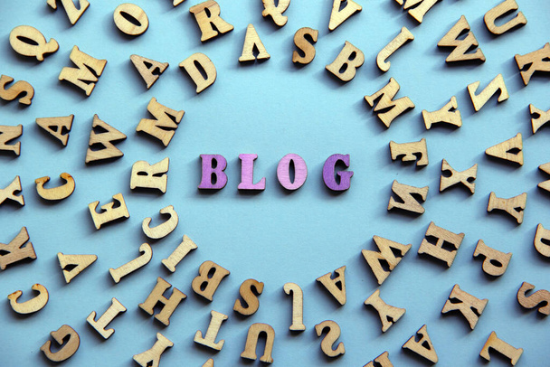 Het paarse woord Blog gemaakt van houten letters, rond vele andere letters op een blauwe achtergrond. Blog woord concept. Bovenaanzicht, vlak lay. - Foto, afbeelding