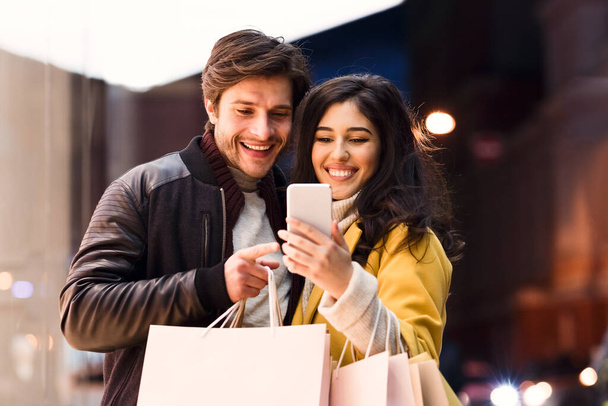 Loving couple using phone after shopping in mall - Photo, Image