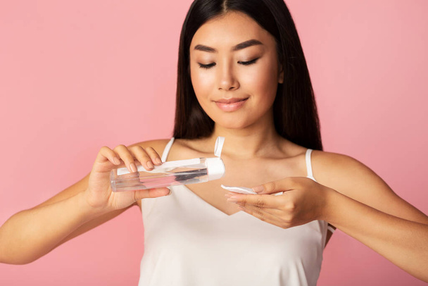 Girl Applying Lotion On Cotton Pad Over Pink Studio Background - Foto, imagen