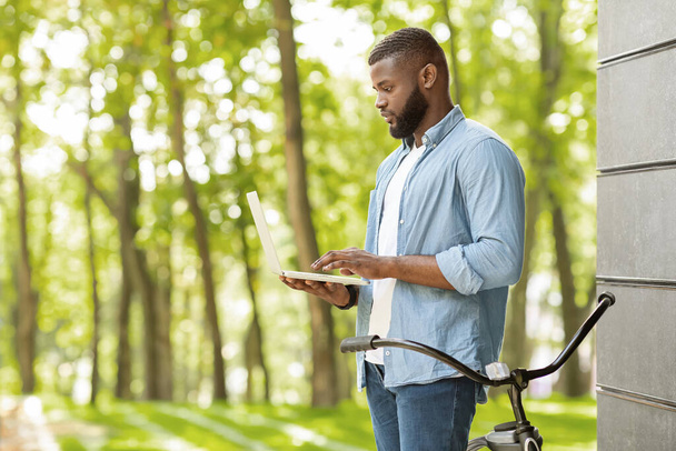 Handsome Black Guy Standing With Laptop Outdoors In Park, Checking Wifi - Zdjęcie, obraz