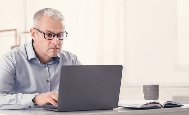 Серйозний старший чоловік використовує ноутбук вдома
 - Фото, зображення