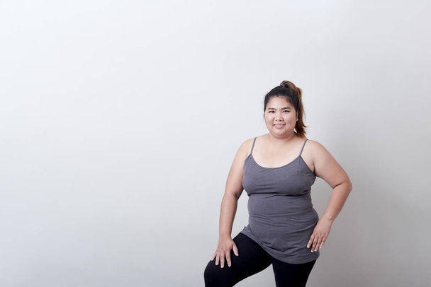 Beautiful fashionable plump asian woman in exercise clothes standing on isolated bright grey background, Healthy exercise concept - Фото, изображение