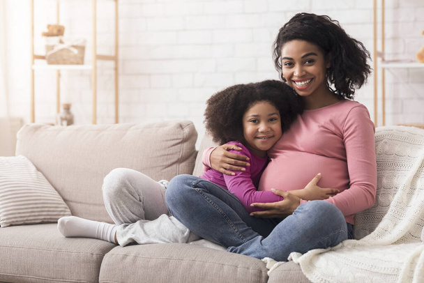 Felice aspettarsi afro donna abbracciare con la sua piccola figlia a casa
 - Foto, immagini