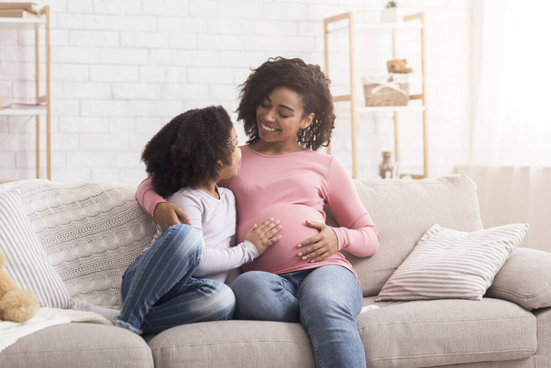 Onnellinen raskaana afro nainen rentoutumassa sohvalla hänen pienen tyttärensä kanssa
 - Valokuva, kuva