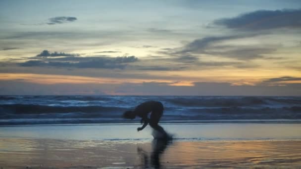 Silhouette Athlete man practicing workout on the beach at sunset. The athlete does a back somersault and does push-ups against the background of the ocean and sunset. - Filmmaterial, Video