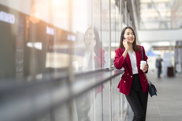 young office worker girl holding hot espresso paper cup leisurely walking on glass wall background thinking about work planning relax during lunch break time. - Photo, image