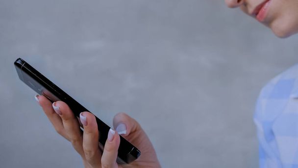 Mujer usando smartphone en habitación gris - vista lateral de cerca
 - Foto, Imagen