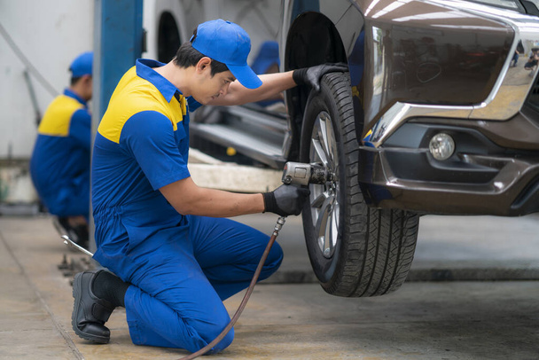 Mecánico asiático cambiando rueda de coche en taller de reparación de automóviles por herramienta de pistola de aire
. - Foto, Imagen