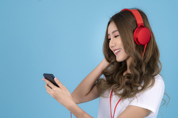 Aziatische vrouw met koptelefoon en het luisteren naar muziek op een blauwe geïsoleerde achtergrond - Foto, afbeelding
