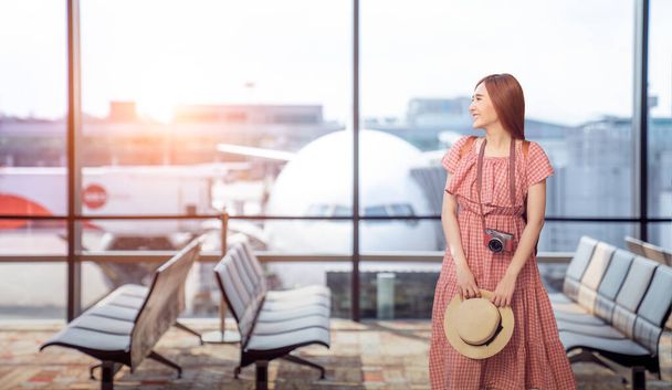 Travel tourist standing with luggage watching sunset at airport window. Unrecognizable woman looking at lounge looking at airplanes while waiting at boarding gate before departure. Travel lifestyle. - Photo, Image