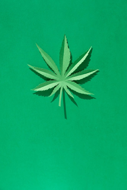 A hemp leaf cut out of paper on a green background. Symbol. - Foto, afbeelding