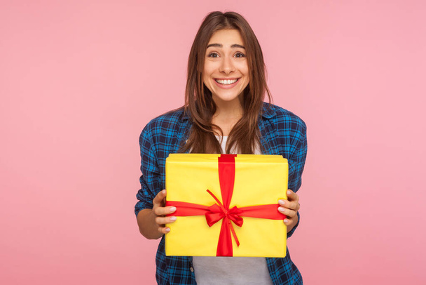Amazing bonus, holiday present! Portrait of extremely happy girl in checkered shirt holding wrapped box and looking at camera with toothy smile, excited about unexpected gift. studio shot, isolated - Foto, imagen