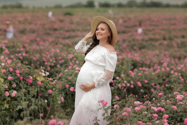 Raskaana oleva nainen olkihattu päässään seisoo kukkapellolla
 - Valokuva, kuva